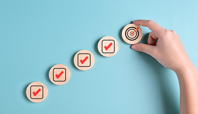Hand placing target icon after checkmarks on wooden discs, symbolizing goal completion and success