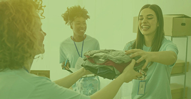 A woman handing a stack of folded clothes to another woman