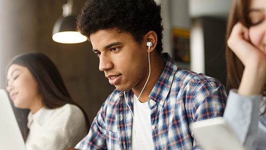 Focused students with laptops and earphones studying in a brightly lit room