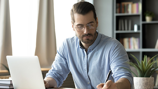 Concentrated man working on a laptop in a well-lit home office with bookshelves